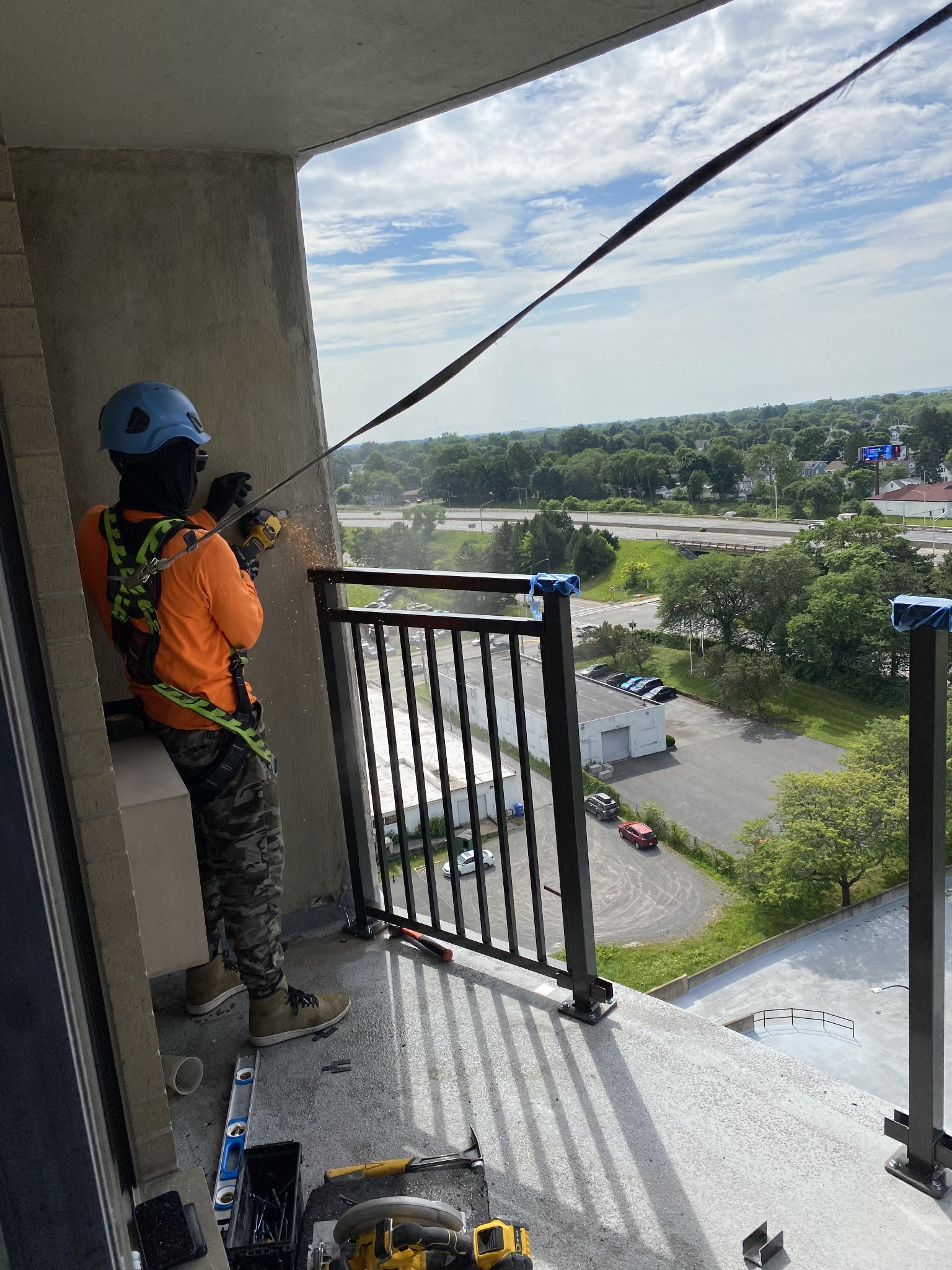 Worker wearing a hard hat and safety harness working beside a balcony railing